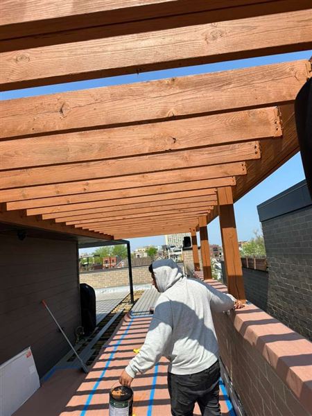 Worker painting wooden pergola rooftop deck completed by NG Construction & Improvements